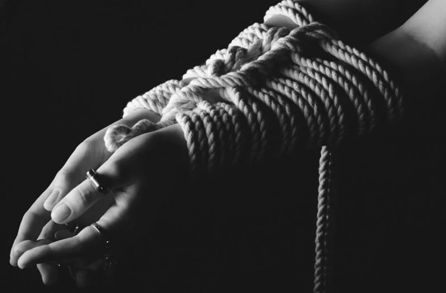 Close up of hand bound with rope in shibari style with detailed knot patterns.