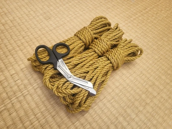 Shibari rope bundle with safety scissors placed on top showing essential rope cutting tool.
